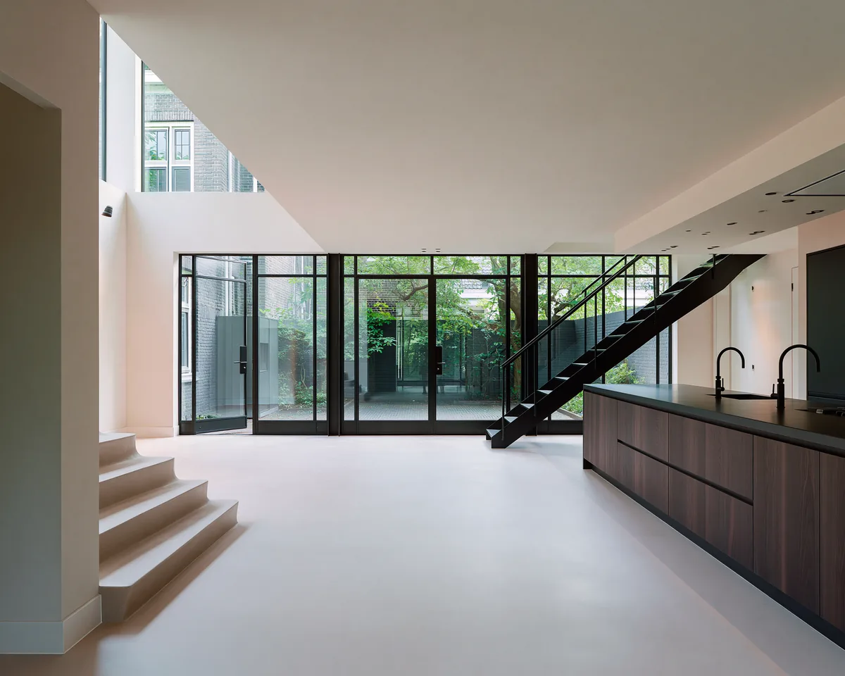 Strak, minimalistisch interieur met een groot naadloos microcement vloervlak en een glaswand naar de binnentuin